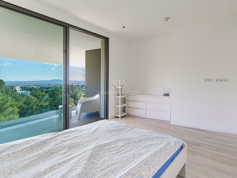 Chambre minimaliste avec grandes portes vitrées ouvrant sur une terrasse avec vue sur la forêt.
