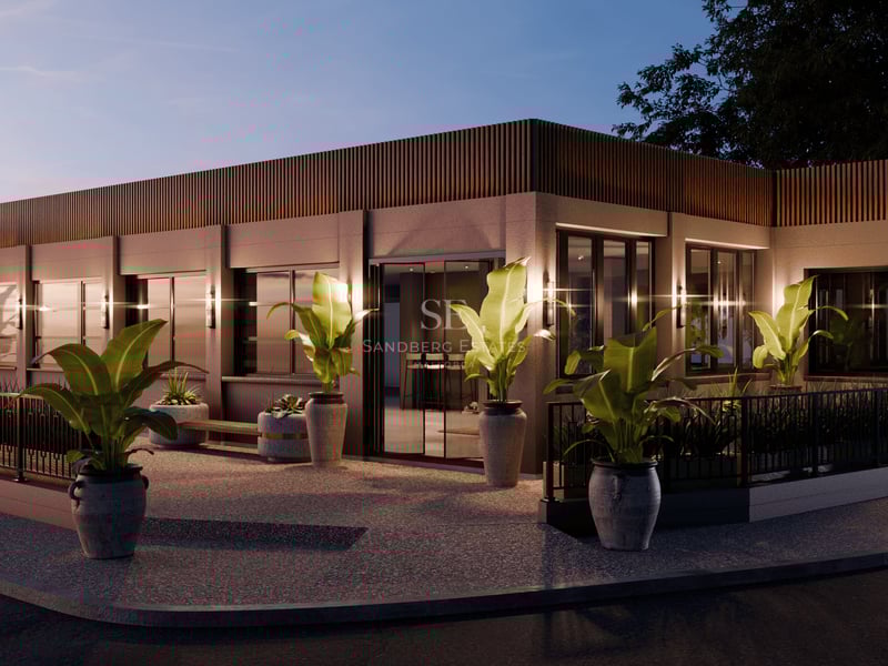 Bâtiment moderne d'un étage au crépuscule avec des lattes de bois, de grandes fenêtres et des plantes tropicales en pot.