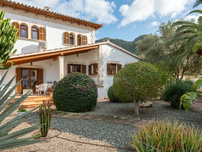 White Mallorcan-style villa with wooden shutters and a succulent garden set against a mountain backdrop.