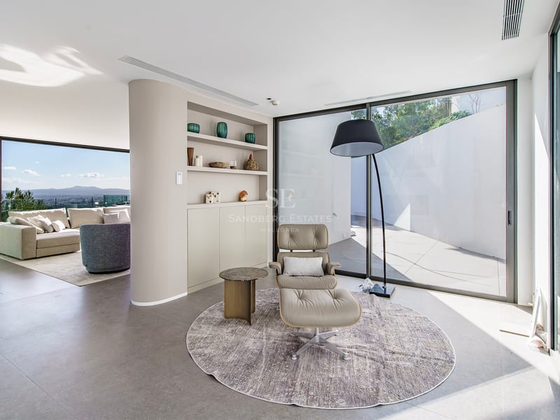 Coin lecture minimaliste avec fauteuil en cuir et baies vitrées offrant une vue sur la ville.