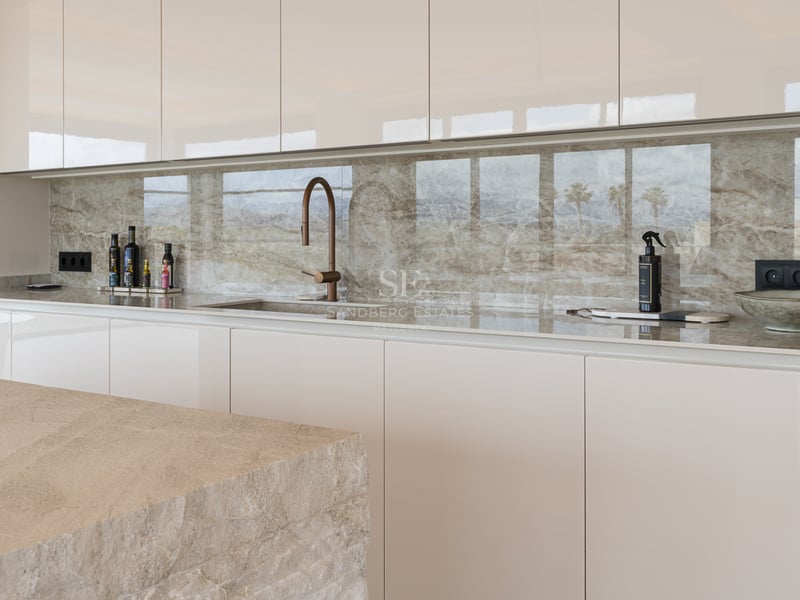 Moderne Küche mit cremefarbenen grifflosen Schränken, gemaserter Marmorrückwand und Design-Armatur in Bronze.