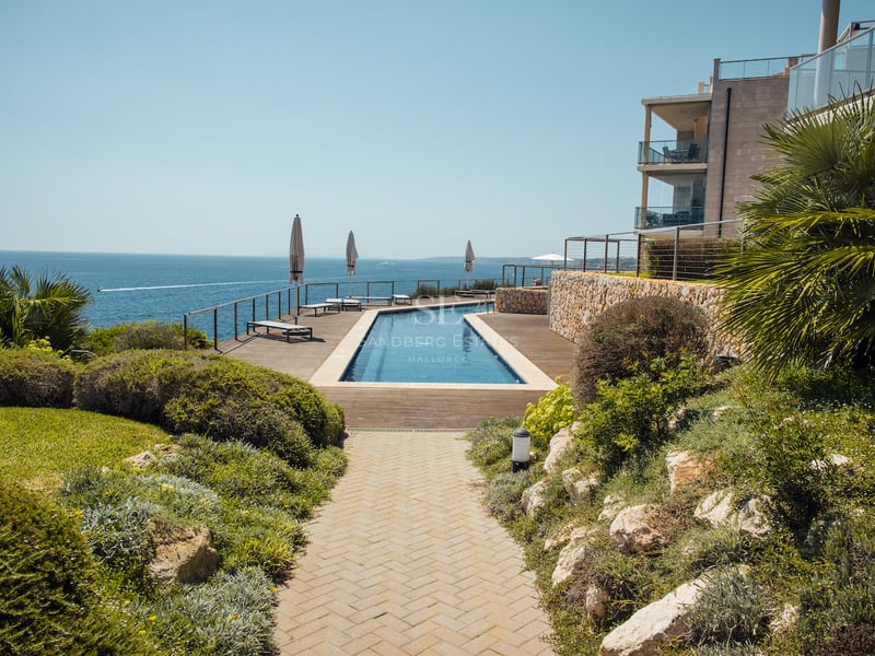 Longue piscine bordée d'une terrasse en bois surplombant la Méditerranée avec des jardins paysagers.