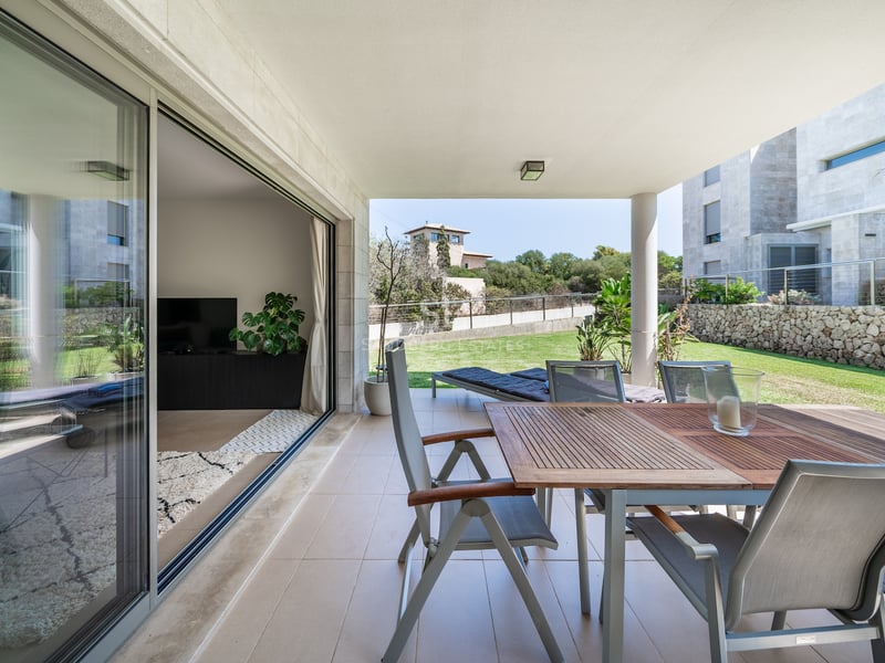 Terrasse couverte avec table à manger en bois et chaises donnant sur une pelouse et un jardin privés.