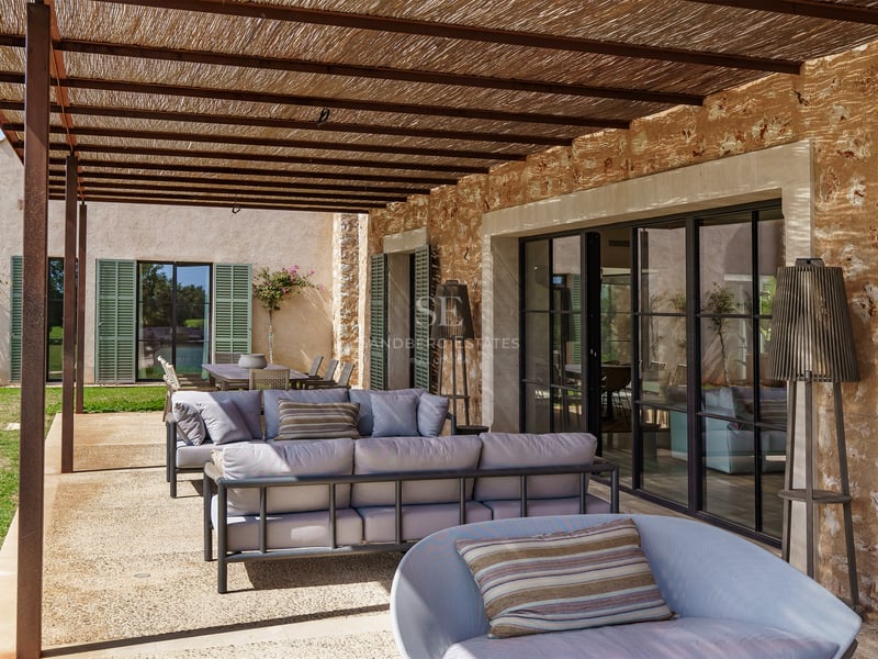 Überdachter Außenbereich mit modernen Sofas, Natursteinwand und Decke mit Holzbalken.