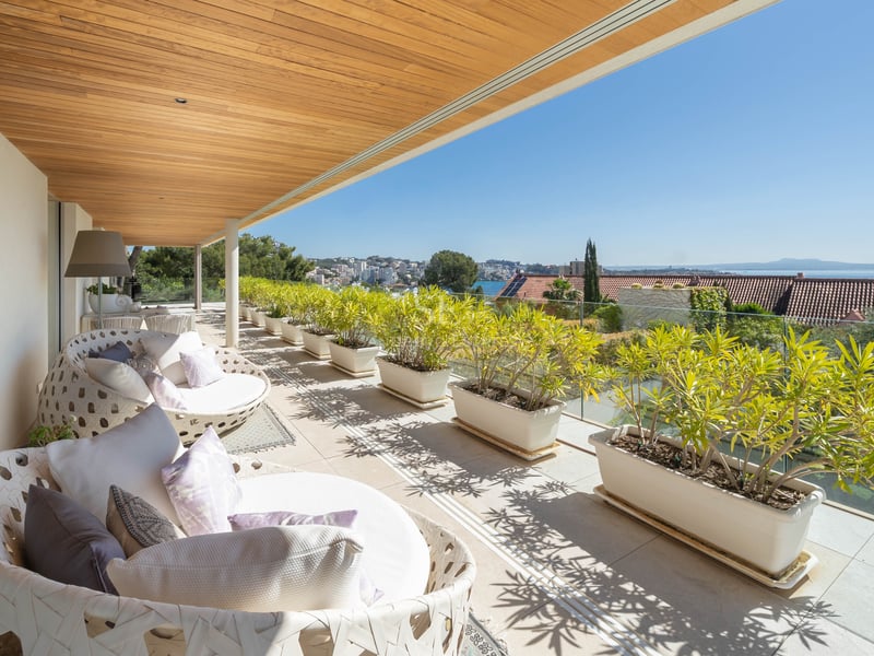 Moderne überdachte Terrasse mit Holzdecke, weißen Loungemöbeln und Pflanzkübeln mit Blick auf das Meer.