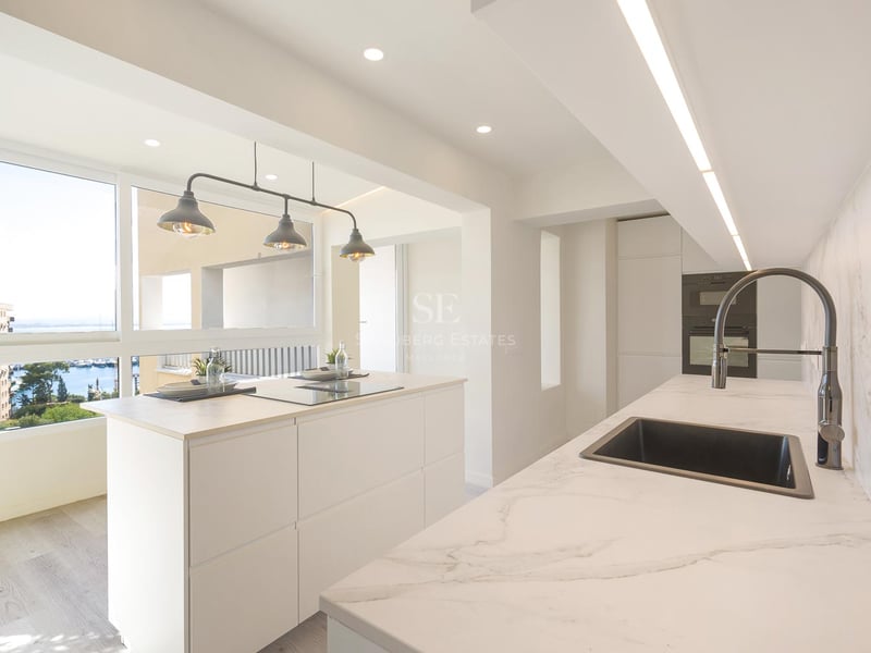 Helle moderne Küche mit weißer Kochinsel, Marmor-Arbeitsplatten und Fenster mit Blick auf einen Yachthafen.