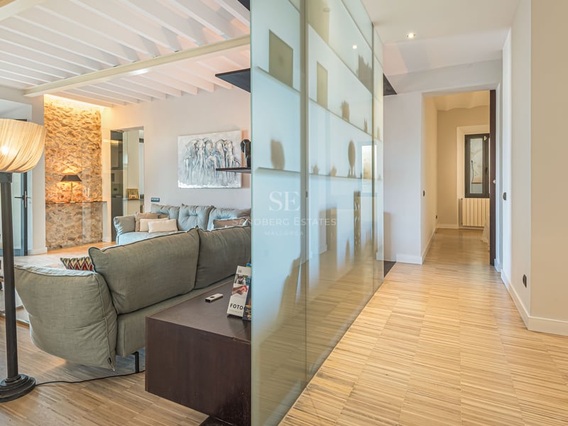 Vardagsrum med grå soffa, trägolv, stenvägg och avskärmning i frostat glas.