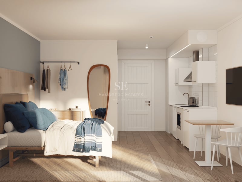 Studio lumineux avec lit aux accents bleus, cuisine blanche compacte et parquet en bois clair.