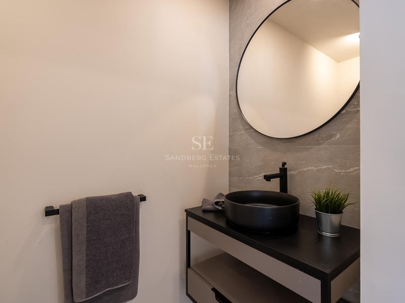 Modernes Badezimmer mit rundem Spiegel, schwarzem Aufsatzwaschbecken und grauen Fliesen in Steinoptik.