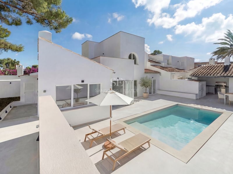 Villa blanche moderne avec piscine rectangulaire, transats et coin repas extérieur sous un toit de tuiles.