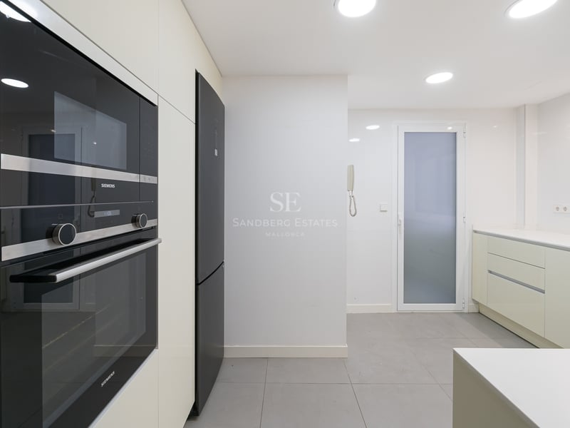 Modernt vitt kök med inbyggda svarta Siemens-vitvaror, grått klinkergolv och infälld belysning.