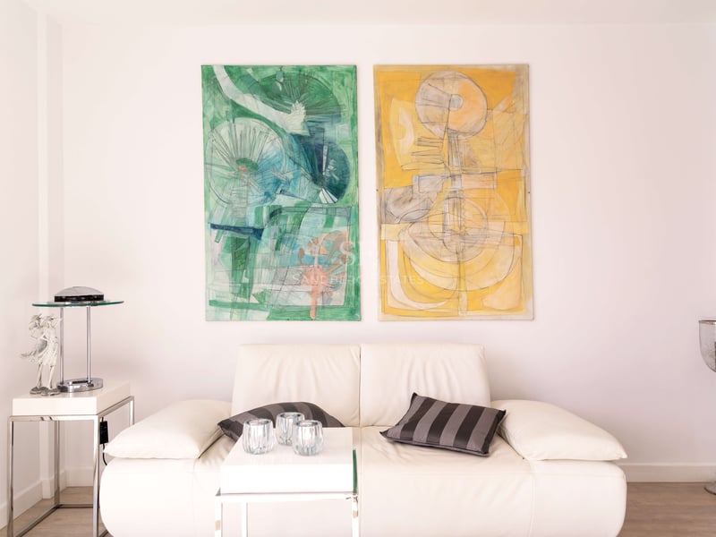 Weißes Ledersofa mit Chromakzenten neben zwei großen abstrakten Gemälden in Grün und Gelb an einer weißen Wand.