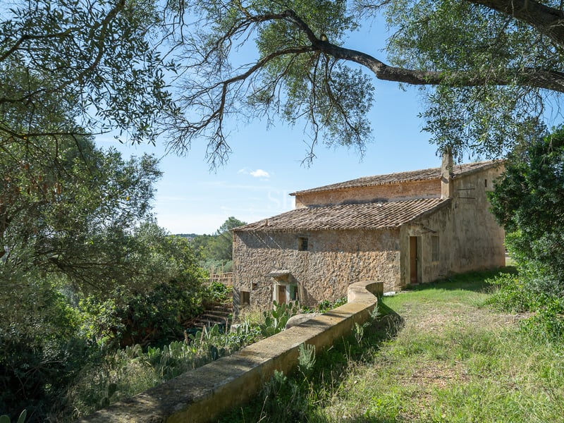 Une maison historique en pierre de deux étages avec un toit en terre cuite entourée d'arbres sous un ciel bleu.