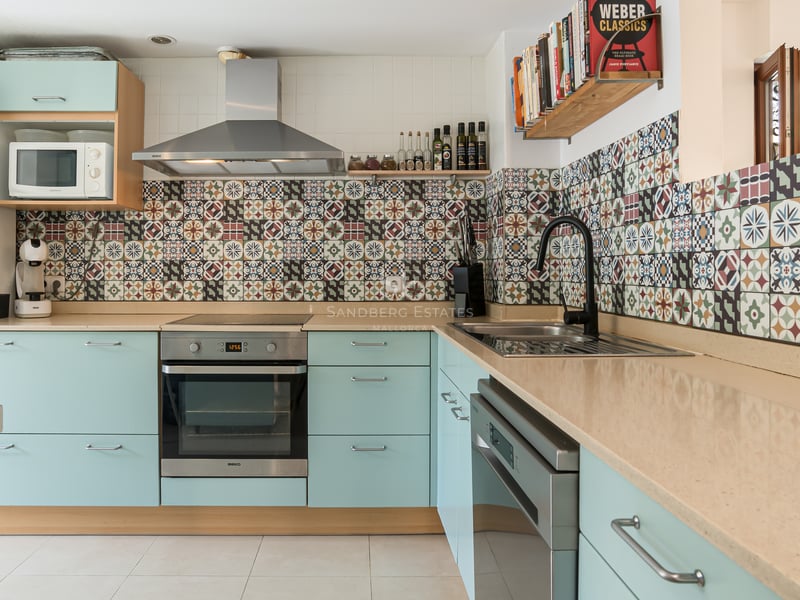 Cuisine avec placards vert menthe, plan de travail beige et crédence en carreaux de ciment colorés.