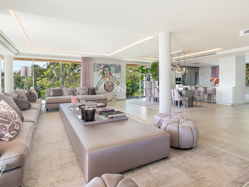 Großzügiger Wohnraum mit hellen Marmorböden, rosa Akzenten und bodentiefen Panoramafenstern zum Garten.