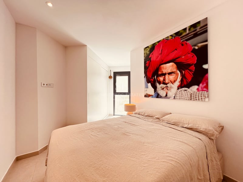 Une chambre moderne dotée d'un grand lit aux draps beiges et d'un portrait coloré au-dessus de la tête de lit.