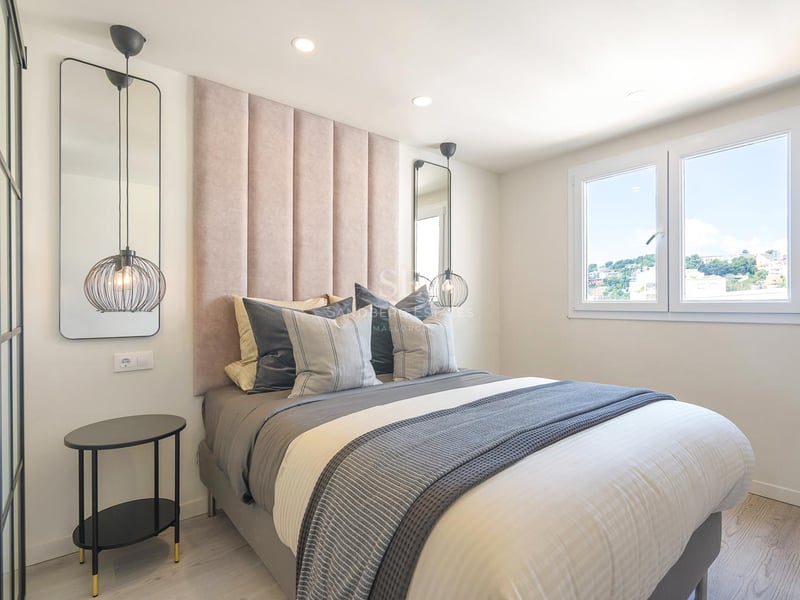 Modernes Schlafzimmer mit altrosafarbenem Kopfteil, Design-Pendelleuchten, grauer Bettwäsche und Fenster.