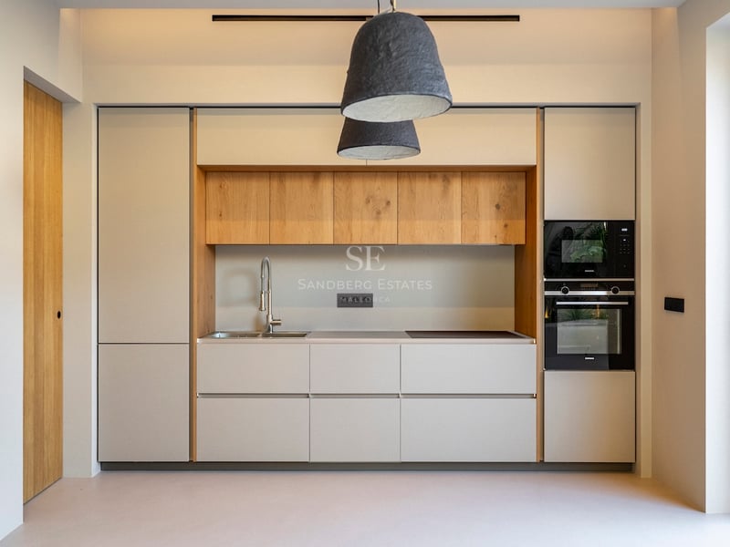 Cuisine moderne aux meubles crème, détails en chêne, appareils intégrés et grandes suspensions texturées.