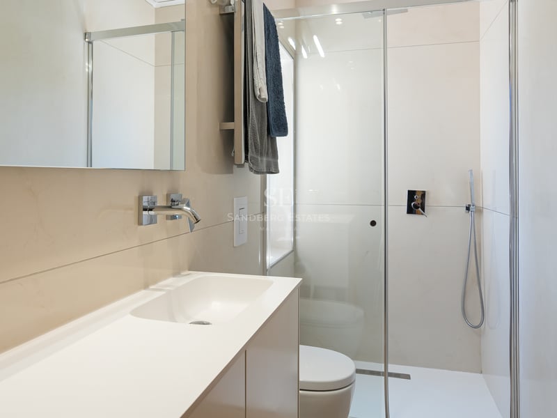 Modernt badrum med beige kakel, duschvägg i glas, vit kommod och kromade detaljer.