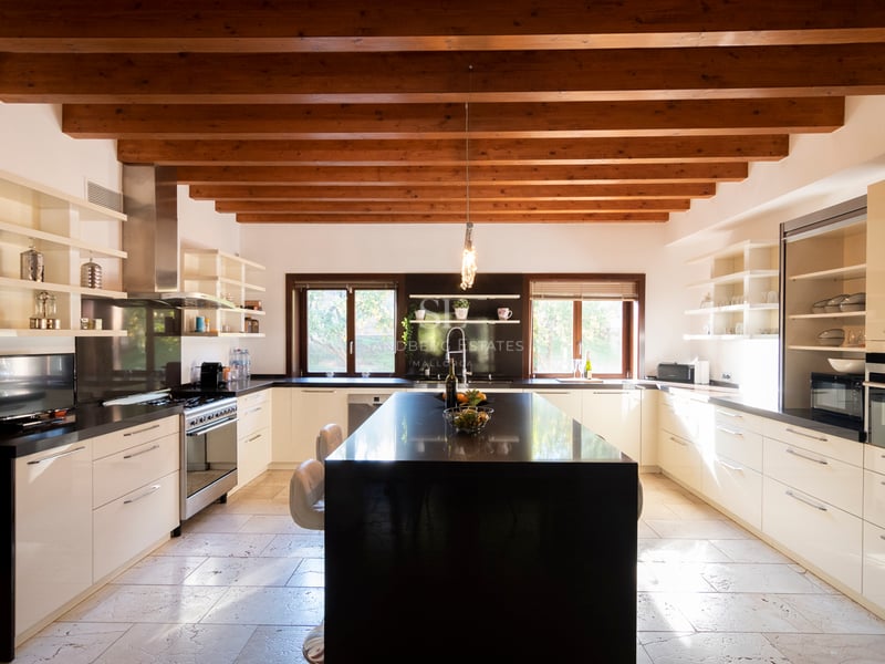 Stort modernt kök med vita skåp, svart granitö och tak med rustika träbjälkar.
