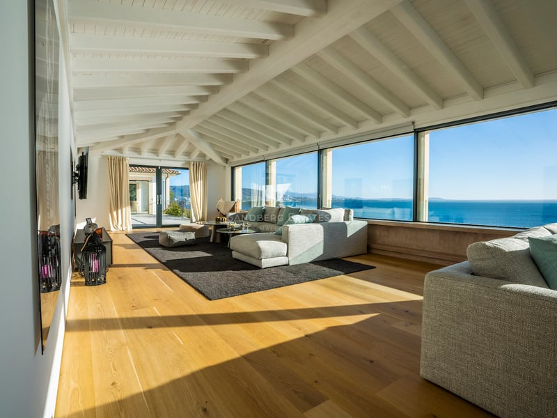Helles Wohnzimmer mit großen Panoramafenstern mit Blick auf das Meer, weißen Balkendecken und Eichenparkett.