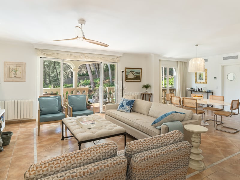 Spacious living room with terracotta floors, cream sofas, fireplace, and glass doors opening to a lush garden.