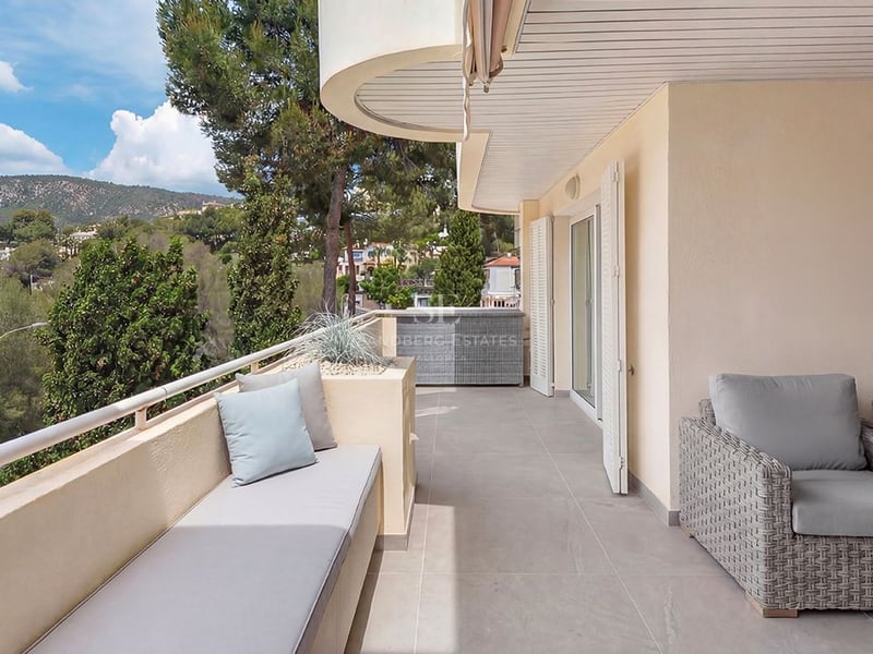 Modern covered terrace with grey rattan furniture, built-in bench seating, and views of lush green hills and pine trees.
