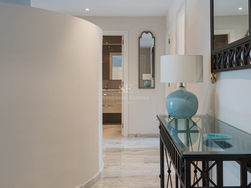 Modern entrance hall featuring a curved wall, polished marble floors, and a glass console table with a blue lamp.