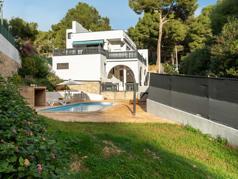 Villa blanche avec piscine privée, terrasse, pelouse et entourée d'une forêt de pins dense.