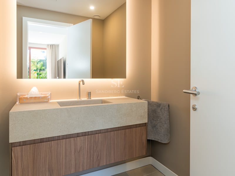 Contemporary bathroom vanity with a backlit mirror, stone countertop, and wood cabinetry in warm taupe tones.
