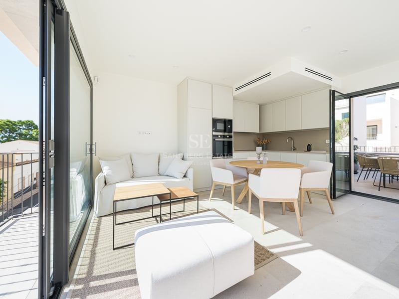 Bright open-plan living and dining room with white furniture, wooden accents, and large glass doors leading to a balcony.