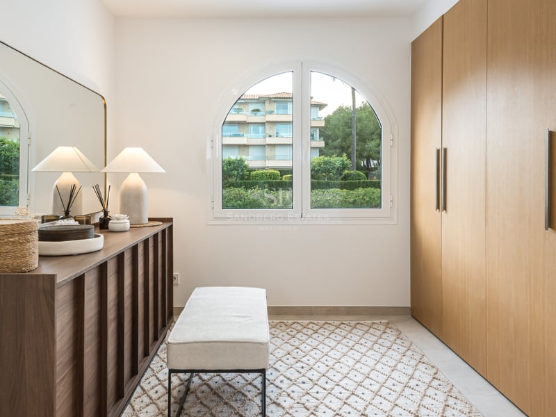 Un dressing moderne avec de grandes armoires en chêne, une fenêtre en plein cintre, une console avec miroir et un banc.