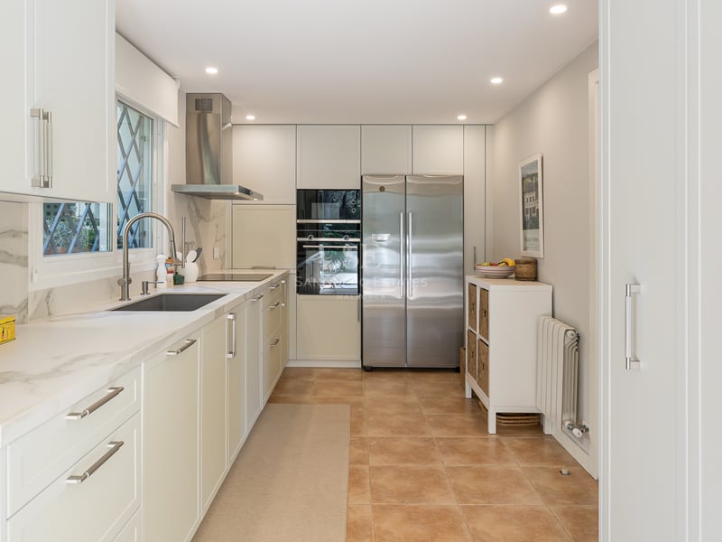 Contemporary galley kitchen featuring white cabinetry, marble countertops, stainless steel appliances, and terracotta floors.