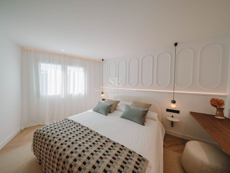 Chambre lumineuse avec un grand lit, des murs blancs décorés de moulures et un parquet en point de Hongrie.