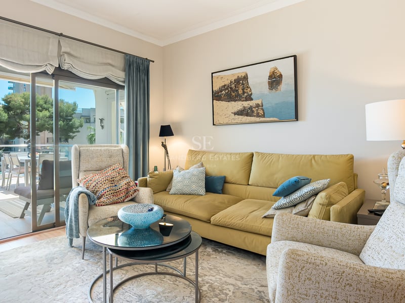 Ljust vardagsrum med senapsgul soffa, mönstrade fåtöljer och skjutdörrar till en solig terrass.