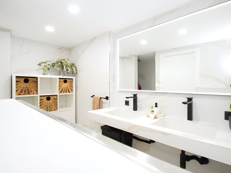 Ljust modernt badrum med dubbelkommod i marmor, mattsvarta kranar och en stor bakgrundsbelyst spegel.