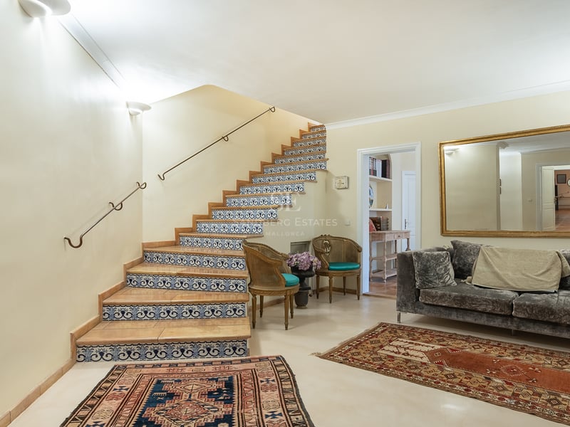 Vue intérieure d'un hall d'entrée avec escalier orné de carreaux bleus et blancs, canapé en velours et tapis.