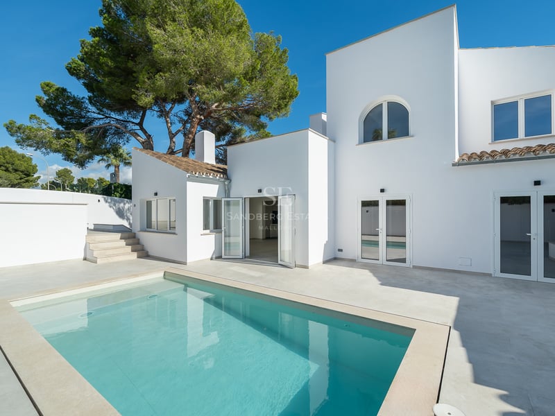Villa blanche moderne avec piscine rectangulaire et terrasse ensoleillée sous un ciel bleu clair.