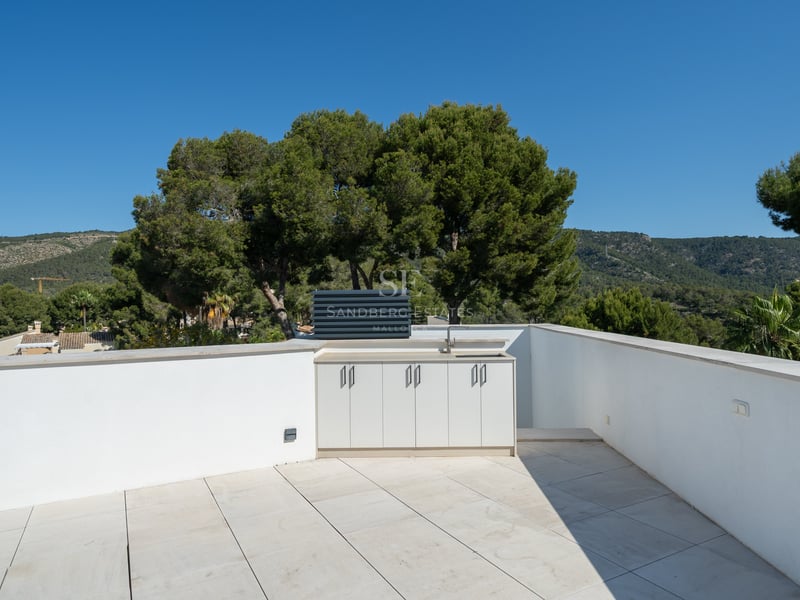 Toit-terrasse aux murs blancs avec une kitchenette extérieure intégrée donnant sur des collines verdoyantes.