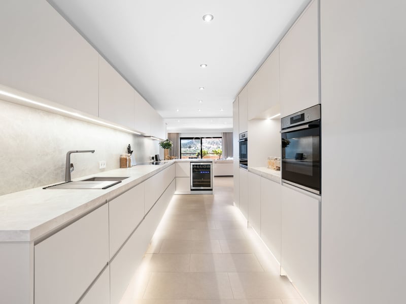 Cuisine moderne avec placards blancs sans poignées, plans de travail en marbre et éclairage LED intégré.