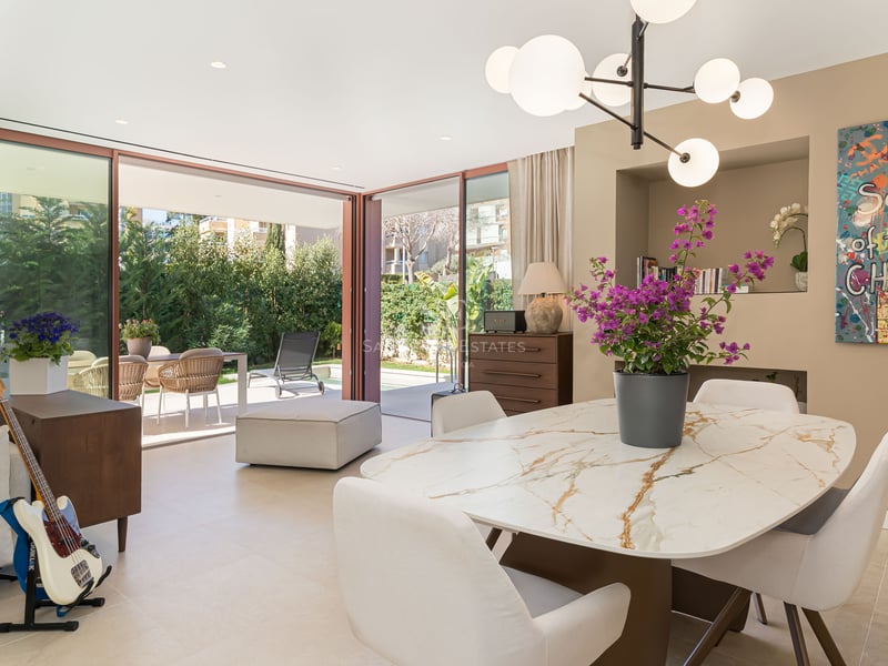 Modern dining area featuring a white marble table, designer pendant light, and floor-to-ceiling glass doors opening to a terrace.