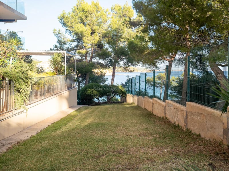 Gepflegter Rasen, umrahmt von Pinien und einem Metallzaun, mit Blick auf das türkisfarbene Mittelmeer.