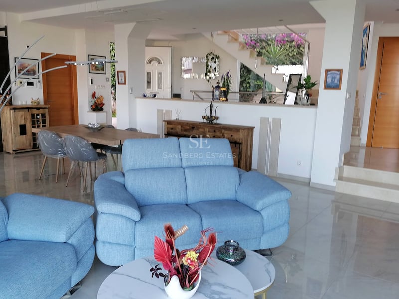 Un grand salon avec des canapés bleus, un sol en marbre poli et un coin repas adjacent dans une villa moderne.