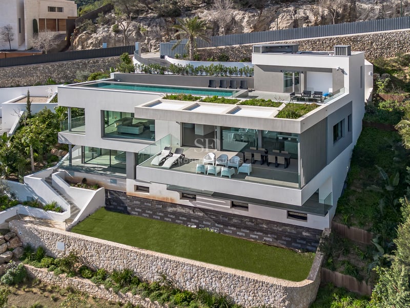 Vue aérienne d'une villa moderne blanche à plusieurs niveaux avec une piscine à débordement sur le toit.
