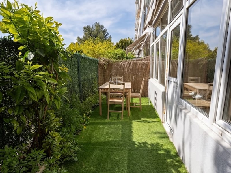 Terraza exterior estrecha con césped artificial verde, conjunto de comedor de madera y vallas de privacidad.