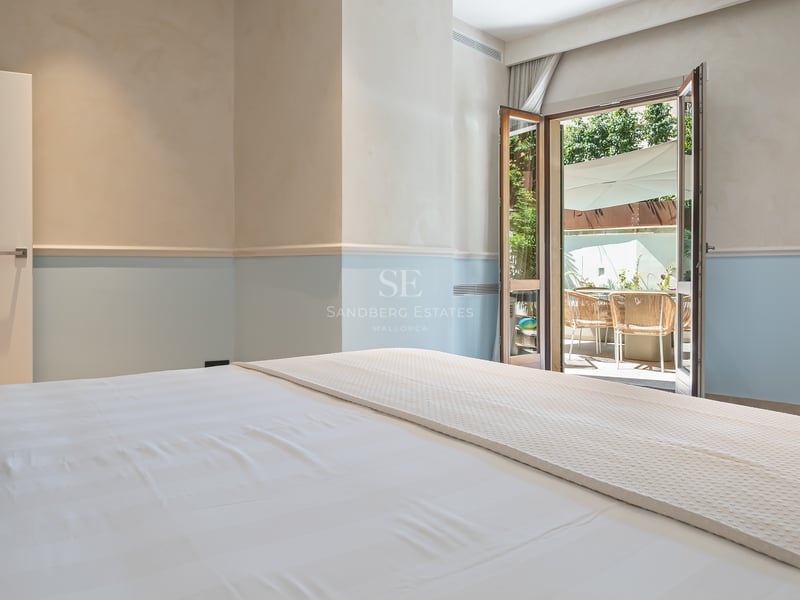 Chambre lumineuse avec linge de lit blanc et murs bleu clair s'ouvrant sur une terrasse ensoleillée.