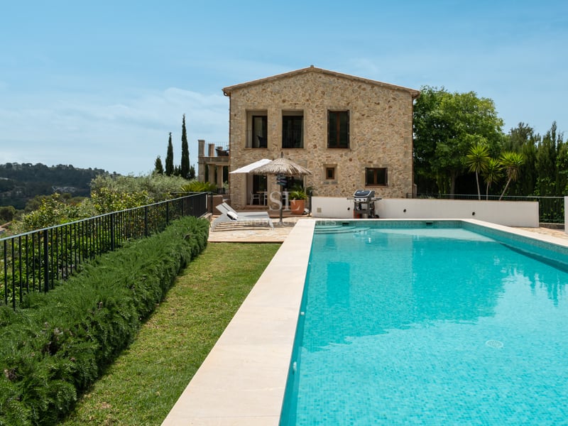 Piscine turquoise et façade en pierre naturelle d'une villa méditerranéenne avec jardin et transats.