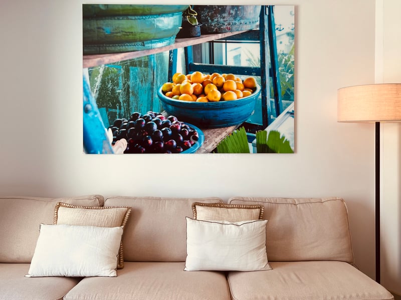 Canapé beige avec coussins décoratifs sous une grande peinture sur toile de fruits dans des bols bleus.