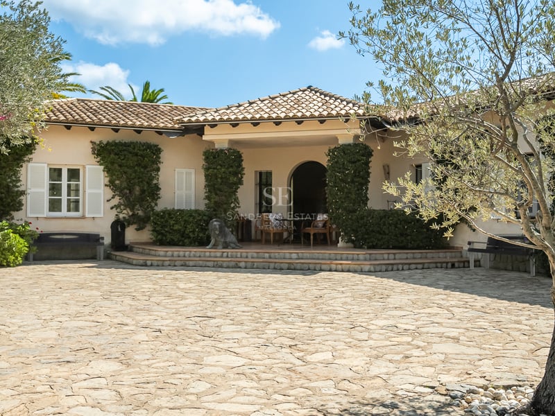 Villa méditerranéenne crème avec toit en terre cuite, volets blancs et une grande cour en pierre naturelle.