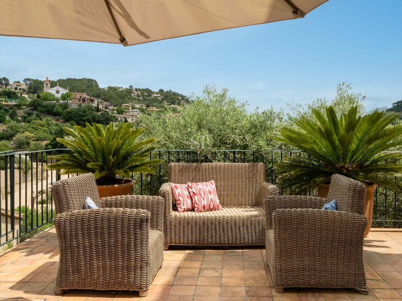 Salon de jardin en osier sur une terrasse en terre cuite avec vue sur les collines méditerranéennes et des villas.